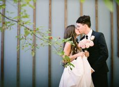 a bride and groom kissing in front of a bamboo fence