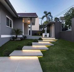 some steps are lit up in front of a house with grass and bushes on the side