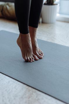 a person standing on a yoga mat in front of a potted plant with their feet up