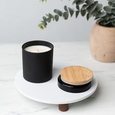 a white table with a black candle on it and a wooden plate next to it