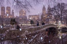 people walking across a bridge over a river in the city at night with snow falling all around