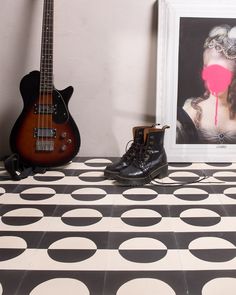 a pair of boots sitting next to a guitar on a tiled floor in front of a framed photograph