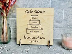 a cake menu sign sitting on top of a counter next to a vase with flowers