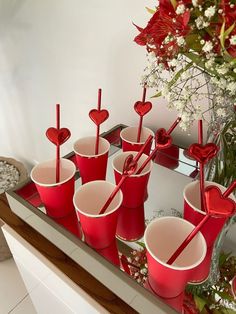 red cups with straws in them are arranged on a mirrored tray next to flowers