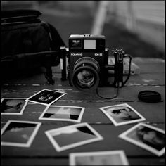 an old camera sitting on top of a wooden table next to pictures and a bag