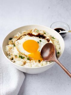 a white bowl filled with rice and an egg on top, next to a wooden spoon