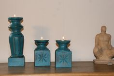 three teal colored candles sitting on top of a wooden shelf next to a statue