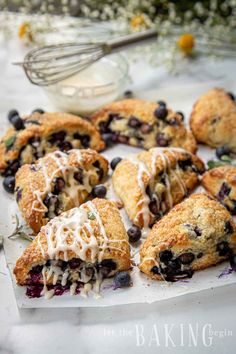 blueberry scones with icing on a white plate next to a bowl of flowers