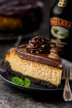 a slice of cheesecake with chocolate frosting on a plate next to a bottle of booze