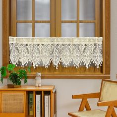 a white lace curtain hanging over a window next to a chair and bookshelf