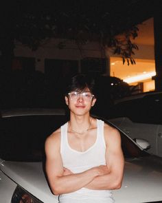 a man standing in front of a white car with his arms crossed and looking at the camera