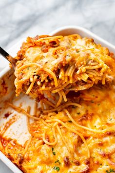 a casserole dish with cheese and meat being scooped from the casserole