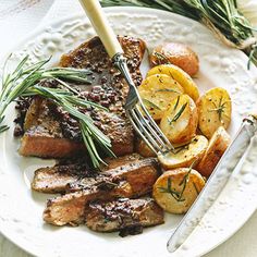 a white plate topped with steak, potatoes and rosemary garnished with seasoning