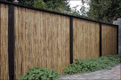 a wooden fence with black posts and green plants growing on it, along side a brick walkway