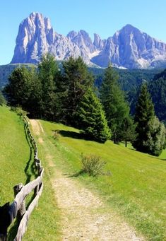 a wooden fence in the middle of a grassy field with mountains in the background on a sunny day