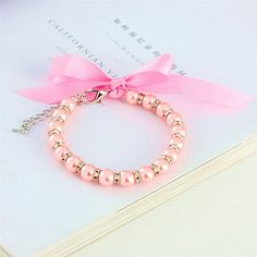 a pink bracelet with pearls and a bow on top of a piece of white paper