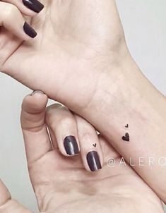 two hands with black nail polishes holding each other's fingers and one has a heart tattoo on it