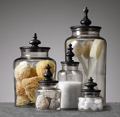 three glass jars filled with different types of bath items on top of a gray surface