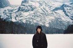 a woman standing in the snow with mountains behind her