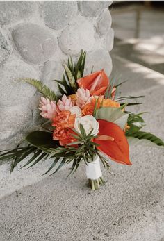 a bouquet of flowers sitting on the ground next to a stone wall with palm leaves