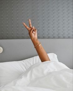 a woman laying in bed making the peace sign with her hand while wearing gold bracelets