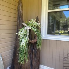 a wreath is hanging on a tree stump in front of a house with the door open