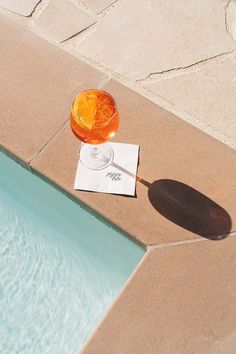 an orange drink sitting on top of a pool next to a paper with the word summer written in it