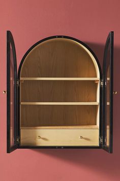 an arched wooden shelf with glass doors on the top and bottom, against a pink wall