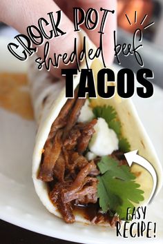 a hand holding a burrito with shredded beef and tacos in it on a white plate