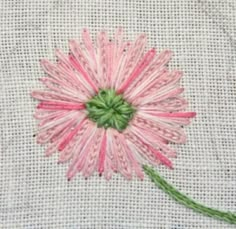 a pink flower is stitched onto a piece of fabric with green thread on it