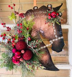 a horse head decorated with red berries and greenery is hanging on a brick wall