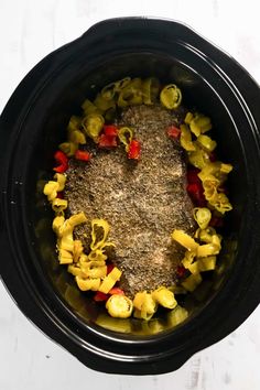 an overhead view of a crock pot filled with pasta and seasoning next to a spoon