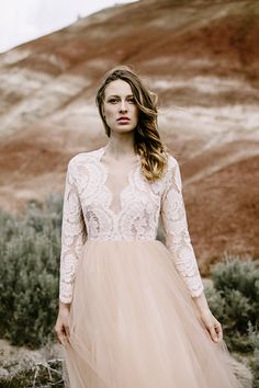 a woman in a dress standing on the side of a hill with her hands behind her back