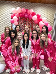 a group of women in pink pajamas posing for a photo with balloons and streamers