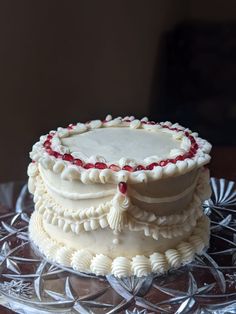 a cake with white frosting and red decorations on a glass platter in front of a brown wall