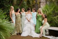 a group of women in dresses standing next to each other on a stone bench surrounded by palm trees