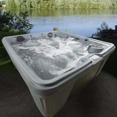 an outdoor hot tub sitting next to a lake with trees in the background and water around it