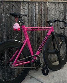 a pink bike parked next to a fence with a stuffed animal on the front wheel