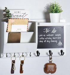 a chalkboard sign hanging on a white wall with key hooks and wallets attached to it