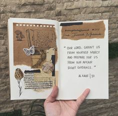 a hand holding up an open book with writing on the pages and paper attached to it