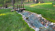 a wooden bench sitting on top of a lush green field next to a small creek