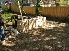 a man standing next to a pile of bags in a yard near a wooden fence