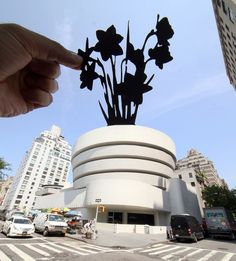 a hand holding up a piece of paper with flowers on it in front of a building