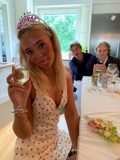 a woman in a polka dot dress holding a wine glass at a table with people