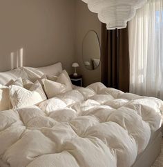 an unmade bed with white sheets and pillows in a bedroom next to a window