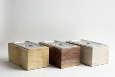 three square wooden containers with metal lids on each side, one in wood and the other in silver