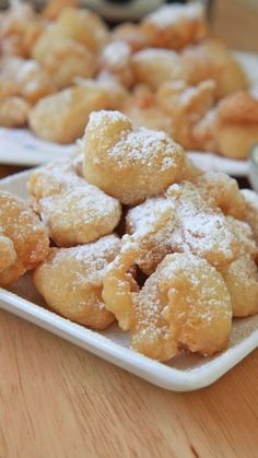 two plates filled with sugared donuts on top of a wooden table