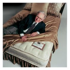 an older man in a suit and tie laying on top of a bed with pillows