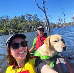 two people on a boat with a dog in the front and trees in the back