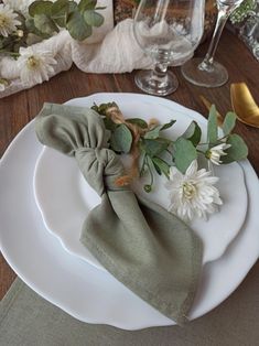 a place setting with napkins and flowers on the plate, along with wine glasses